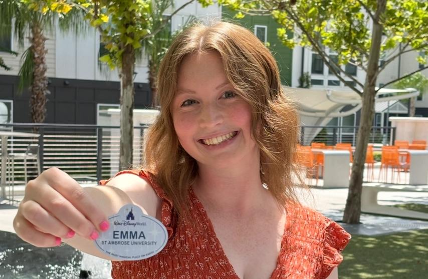 Emma Stiener '26, Elementary Education, smiles into the camera while holding up her Disney College Program name badge,