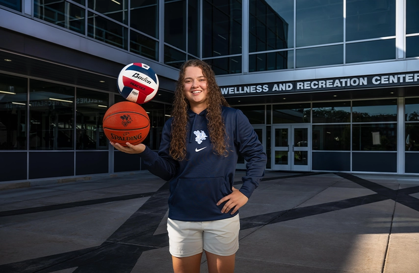 Carrie Hungate, '28, stands in front of the Wellness and Recreation Center at St. Ambrose University and smiles into the camera.
