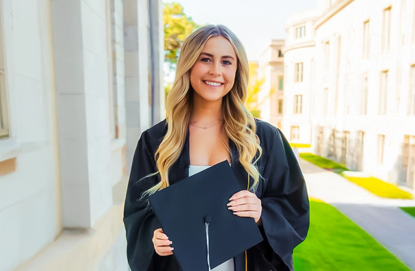Isabelle Matthys smiles at the camera while holding her graduation cap and wearing her graduation gown.
