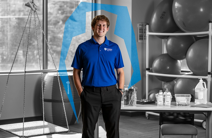 Ivan Hovland smiles into the camera while standing in an Occupational Therapy classroom. He smiles into the camera while a blue Ambrosian arc surrounds him.