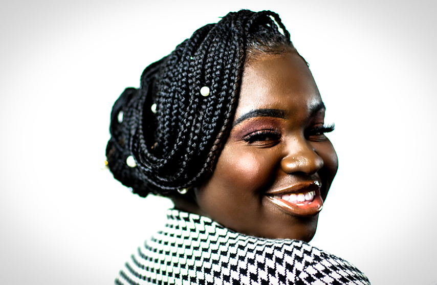 Lydia Amissa-Harris smiles over one shoulder at the camera against a white background.