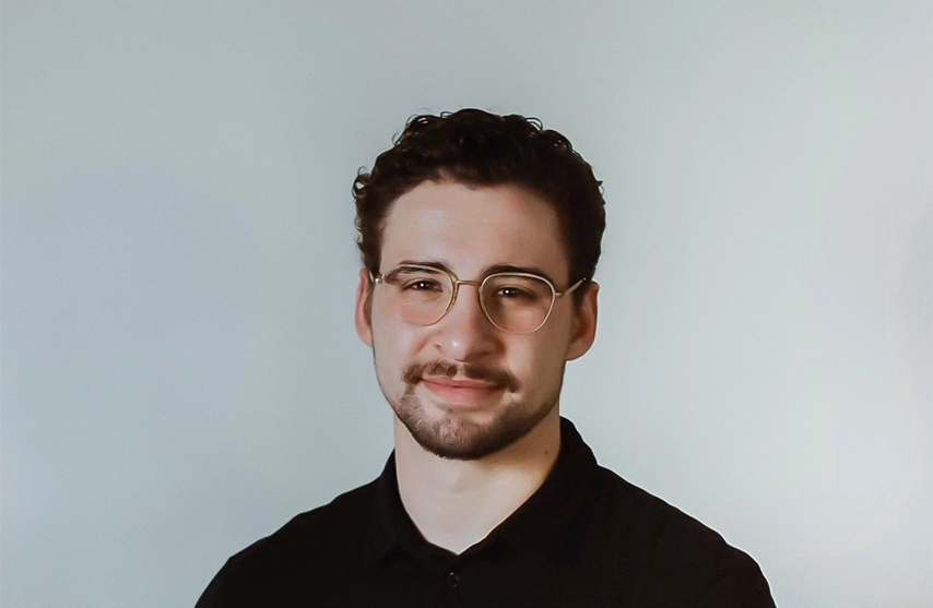 Sam Volkmer smiles into the camera against a grey background.