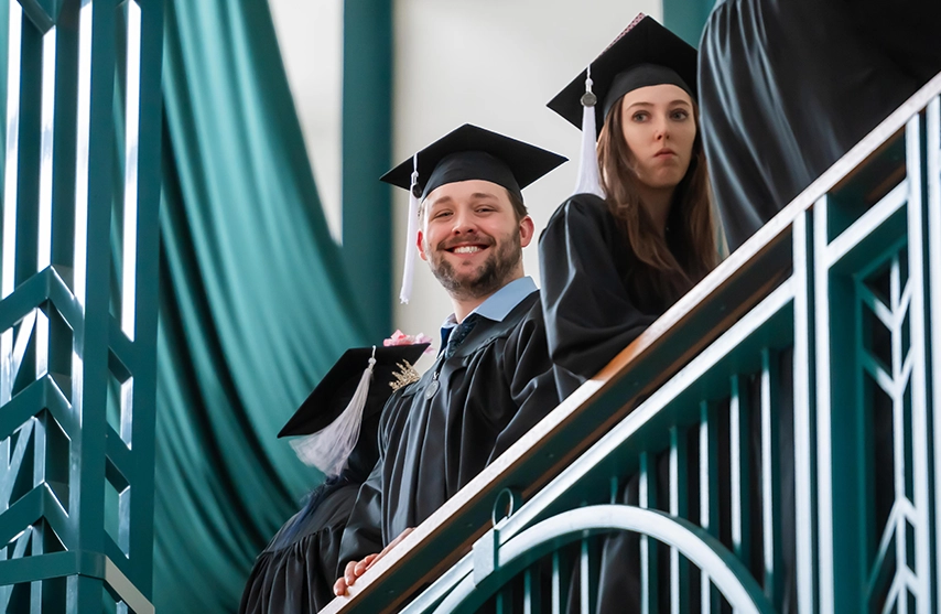 Students stand at the balcony and smile down at the camera during St. Ambrose University's graduation.