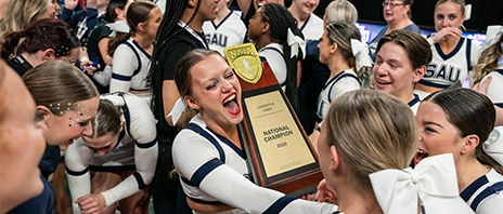 St. Ambrose University's Cheer team smiles in excitement while holding their 2023 First Place trophy at NAIA tournament.