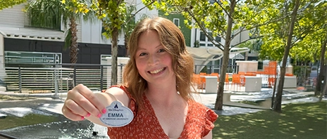 Emma Stiener '26, Elementary Education, smiles into the camera while holding up her Disney College Program name badge,