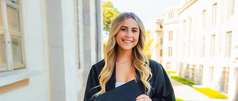 Isabelle Matthys smiles at the camera while holding her graduation cap and wearing her graduation gown.