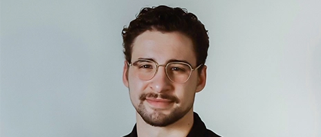 Sam Volkmer smiles into the camera against a grey background.