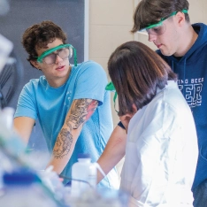 Two students with professor in chemistry lab conducting experiment.