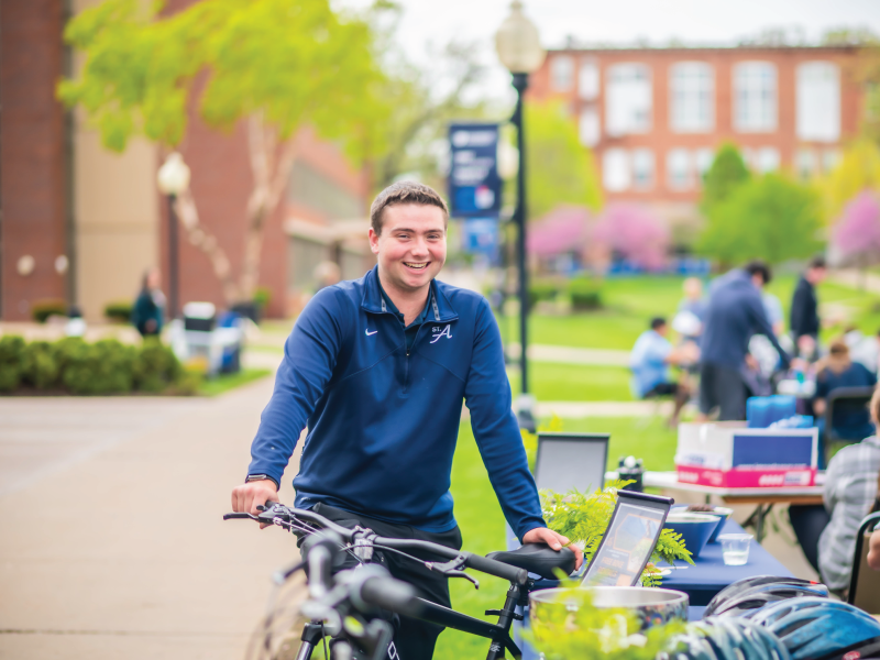 A student with a bicycle in front of grassy area on campus.