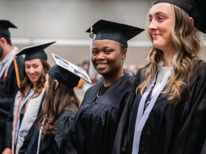 Student smiling at graduation in crowd.