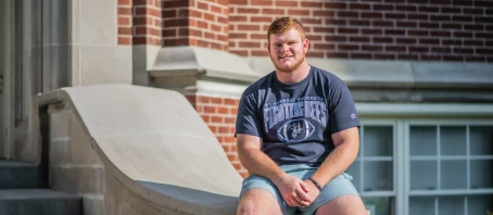 Student athlete sits on steps in front of academic building.