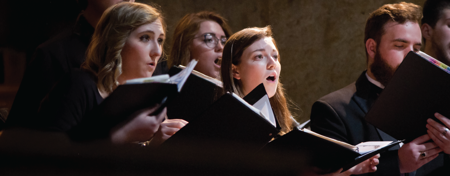 Student singing in a choir onstage at St. Ambrose University.