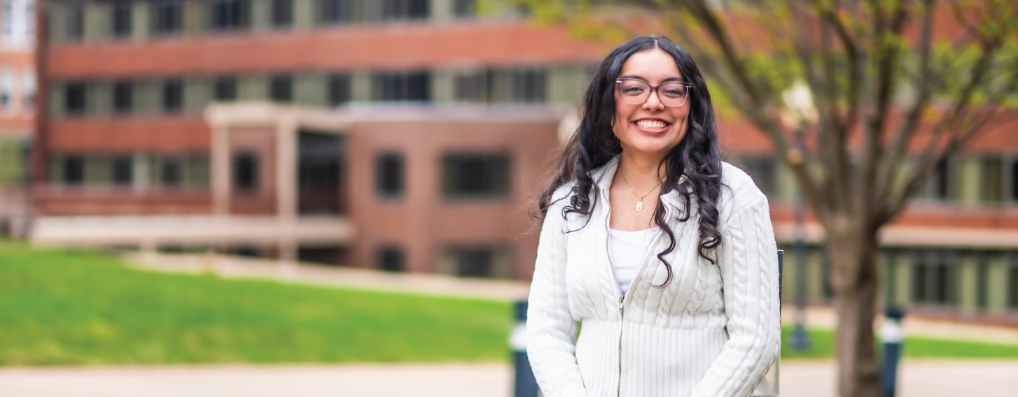 Student stands outdoors in front of brick building.
