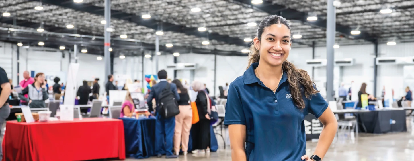 Student standing in front of booths at career fair, smiling.