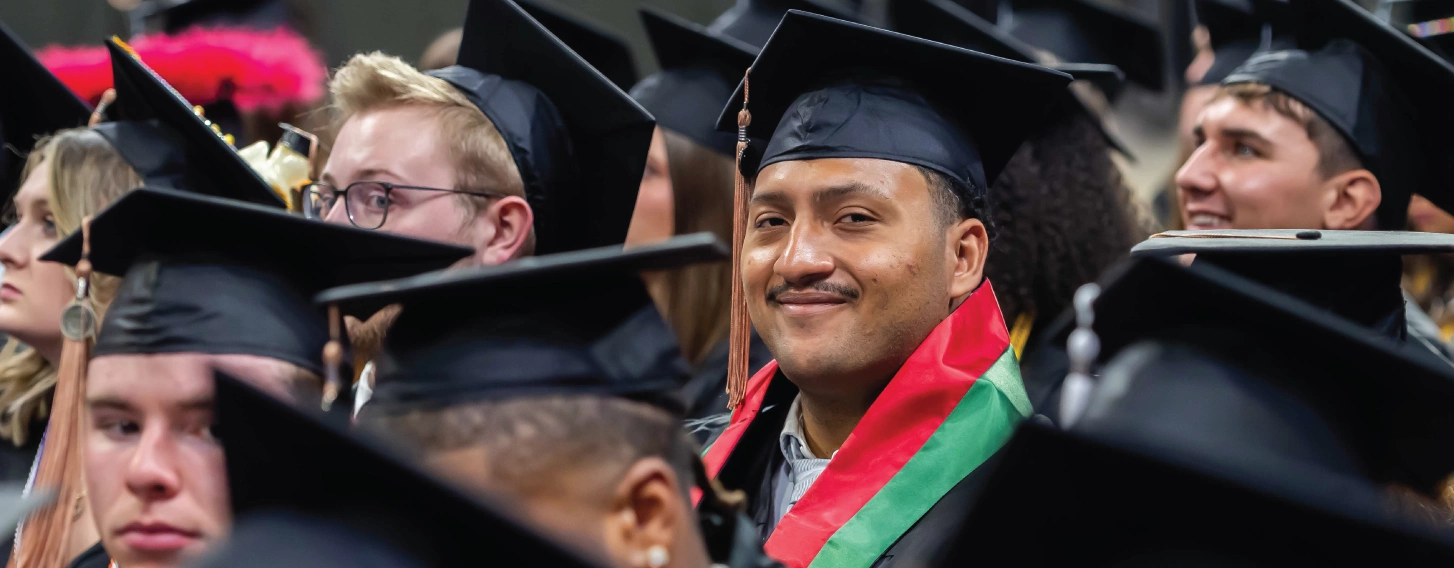 One graduate smiling in a crowd of students at commencement.