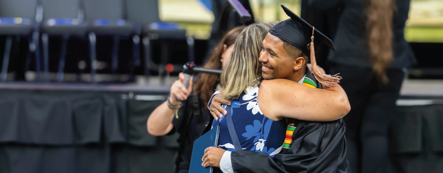 Graduate hugs staff person after receiving diploma.