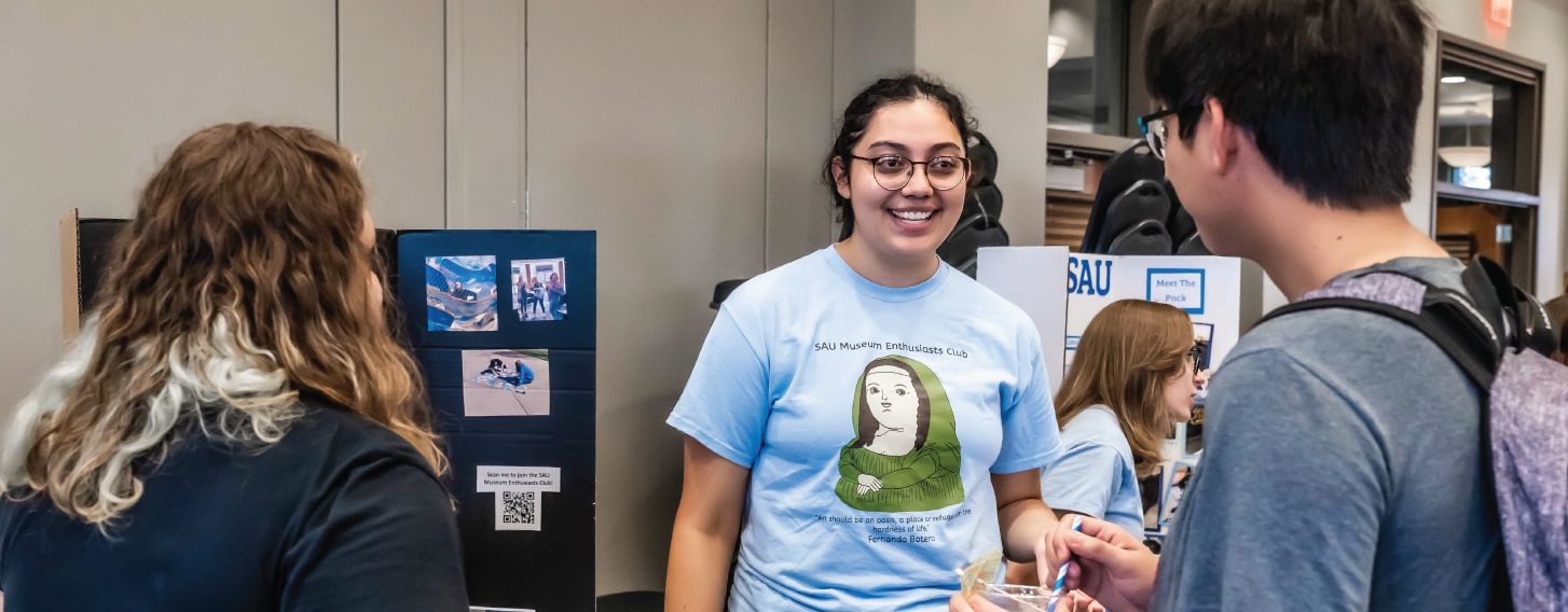 Student smiling indoors at a club fair.