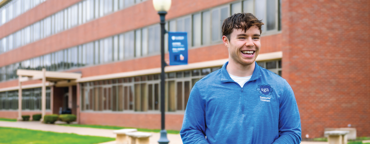 Student standing outside dorm, smiling broadly.