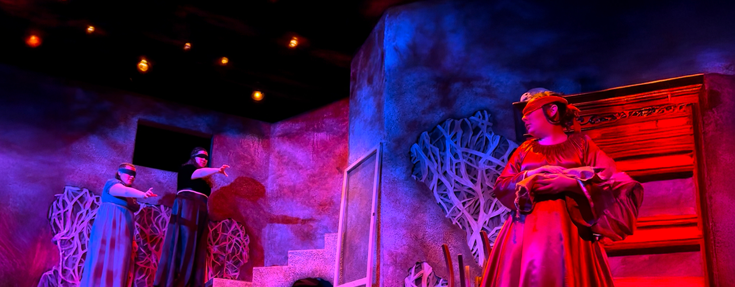 Students cast in a red light recite their lines during a theatre show.