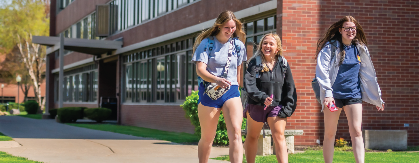 Three students walking on campus on a sunny day.