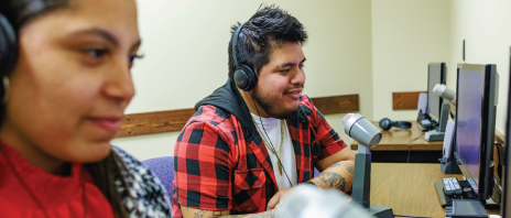 Two students wearing headphones observing a social work exercise with microphones and computers.